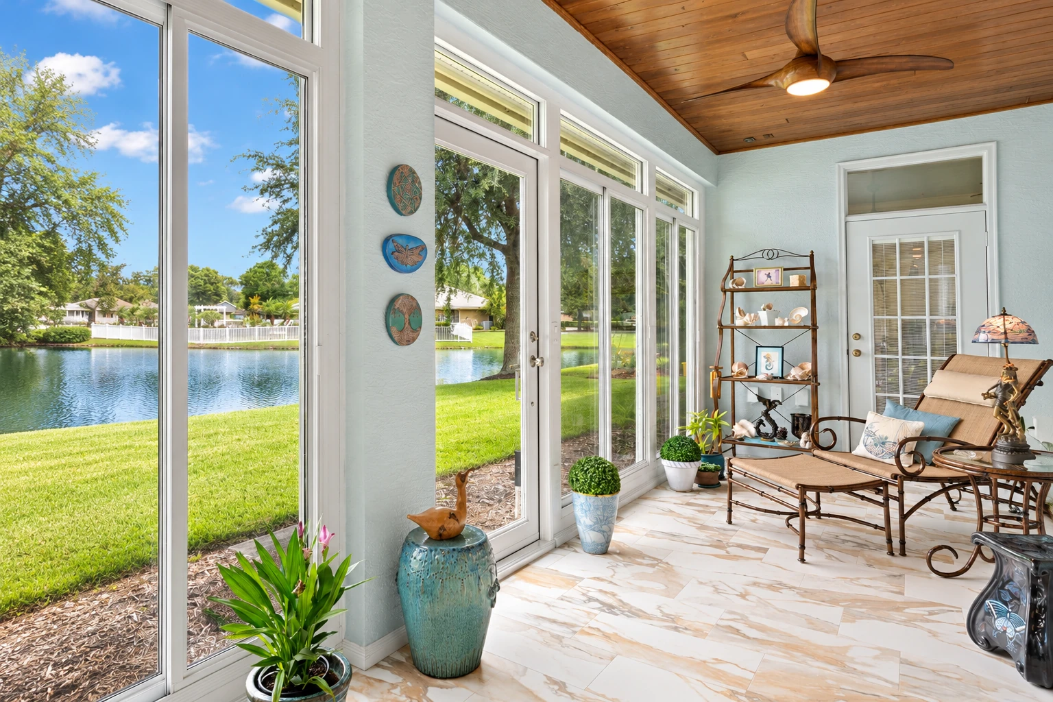Custom sunroom with tall windows, a wood-paneled ceiling, and wicker seating overlooking a grassy lawn and pond.