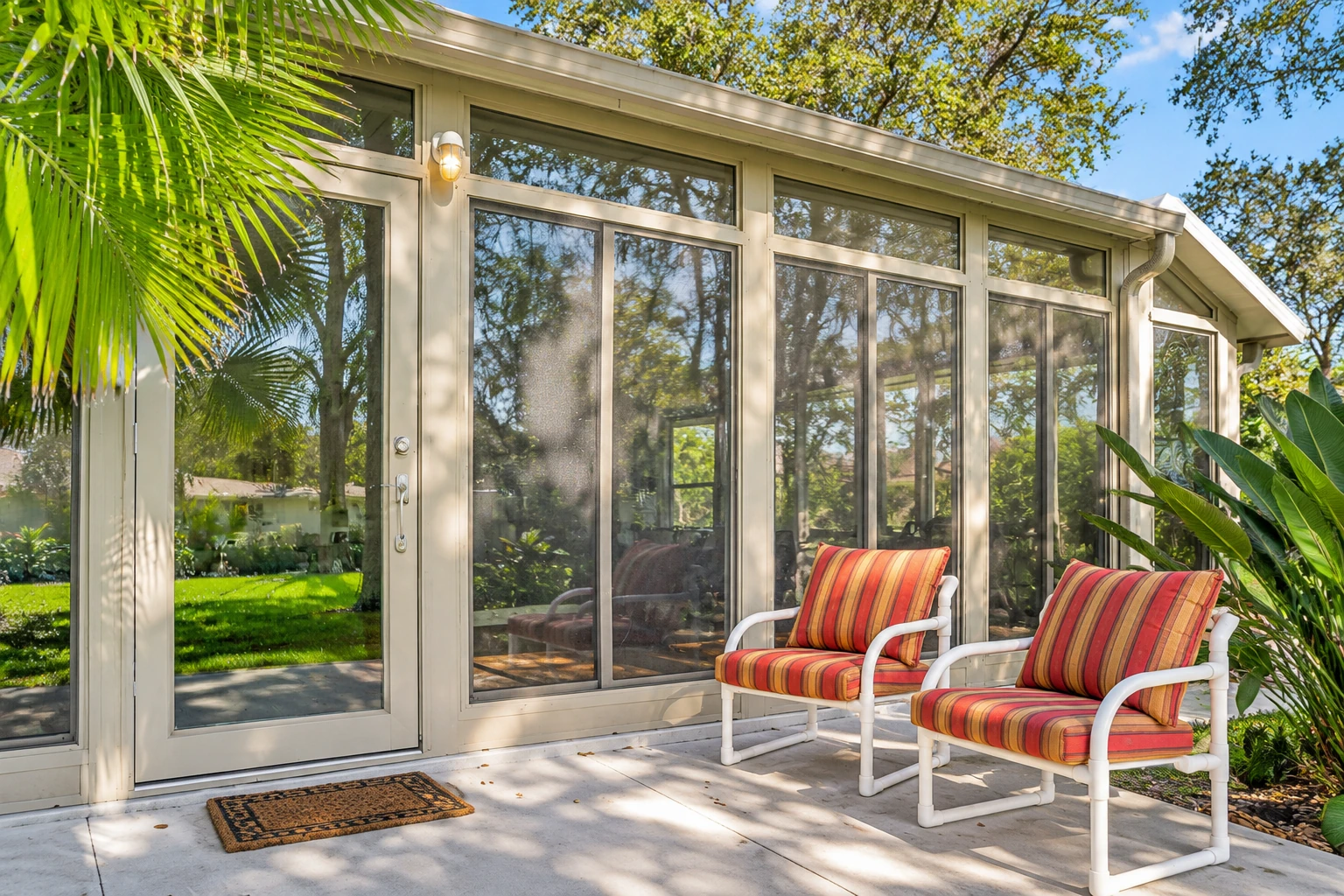 Enclosed patio room with tall glass panels and a white-framed door, beside two striped-cushion chairs.