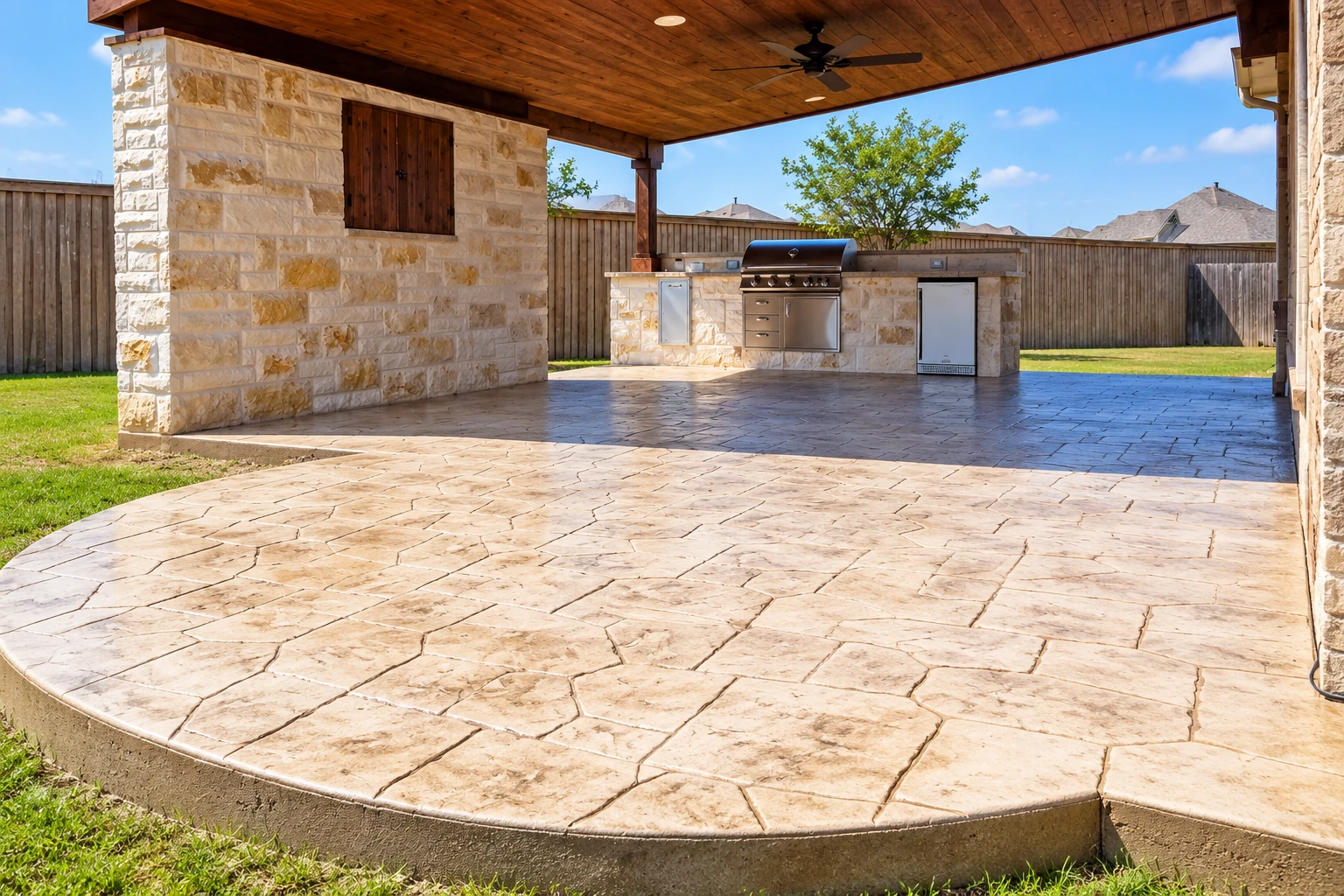 Covered patio with a wood-paneled ceiling, stone outdoor kitchen, and spacious stamped-stone floor.