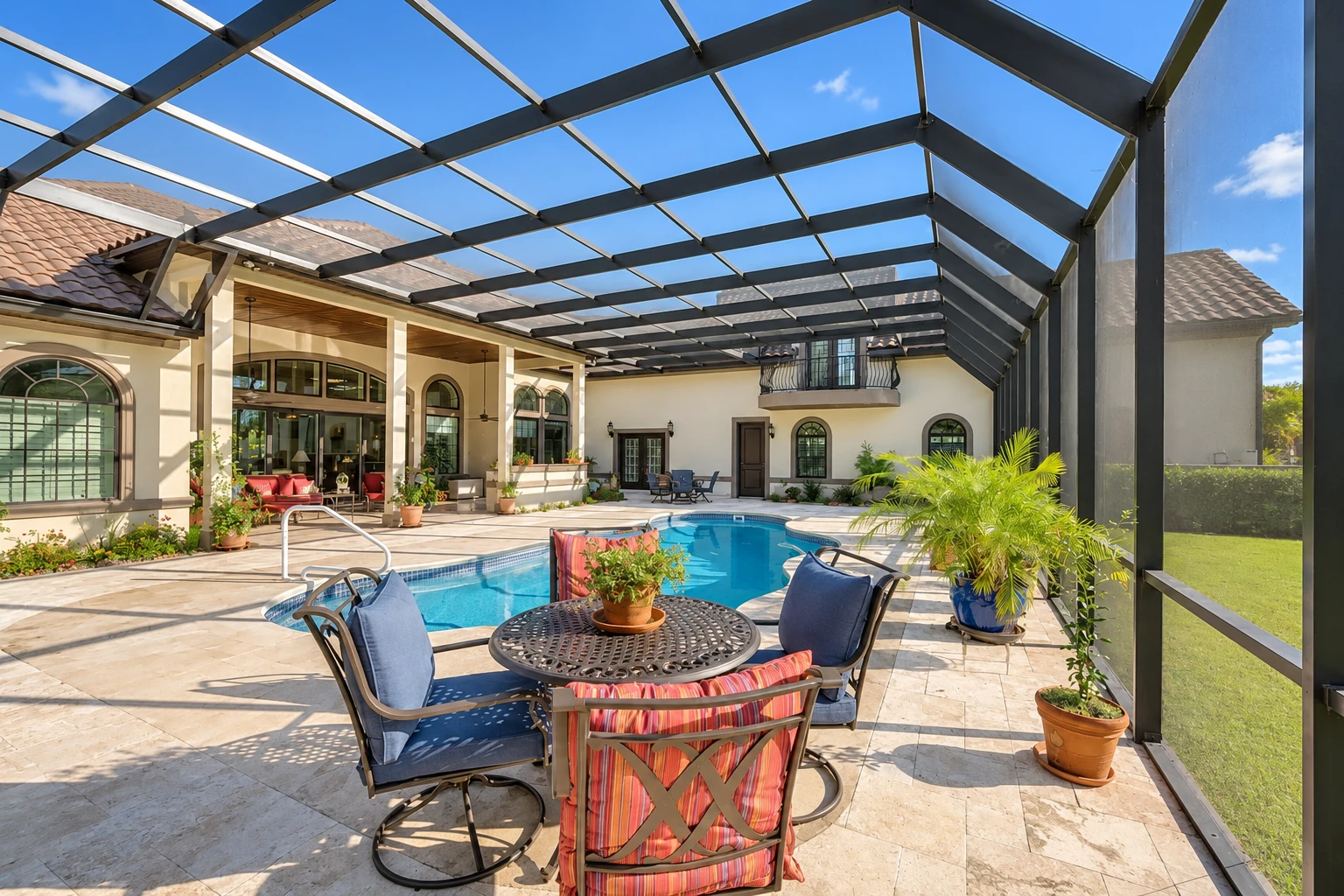 A screened patio enclosure with a dark metal roof frame surrounds a swimming pool and outdoor seating beside a stucco home.