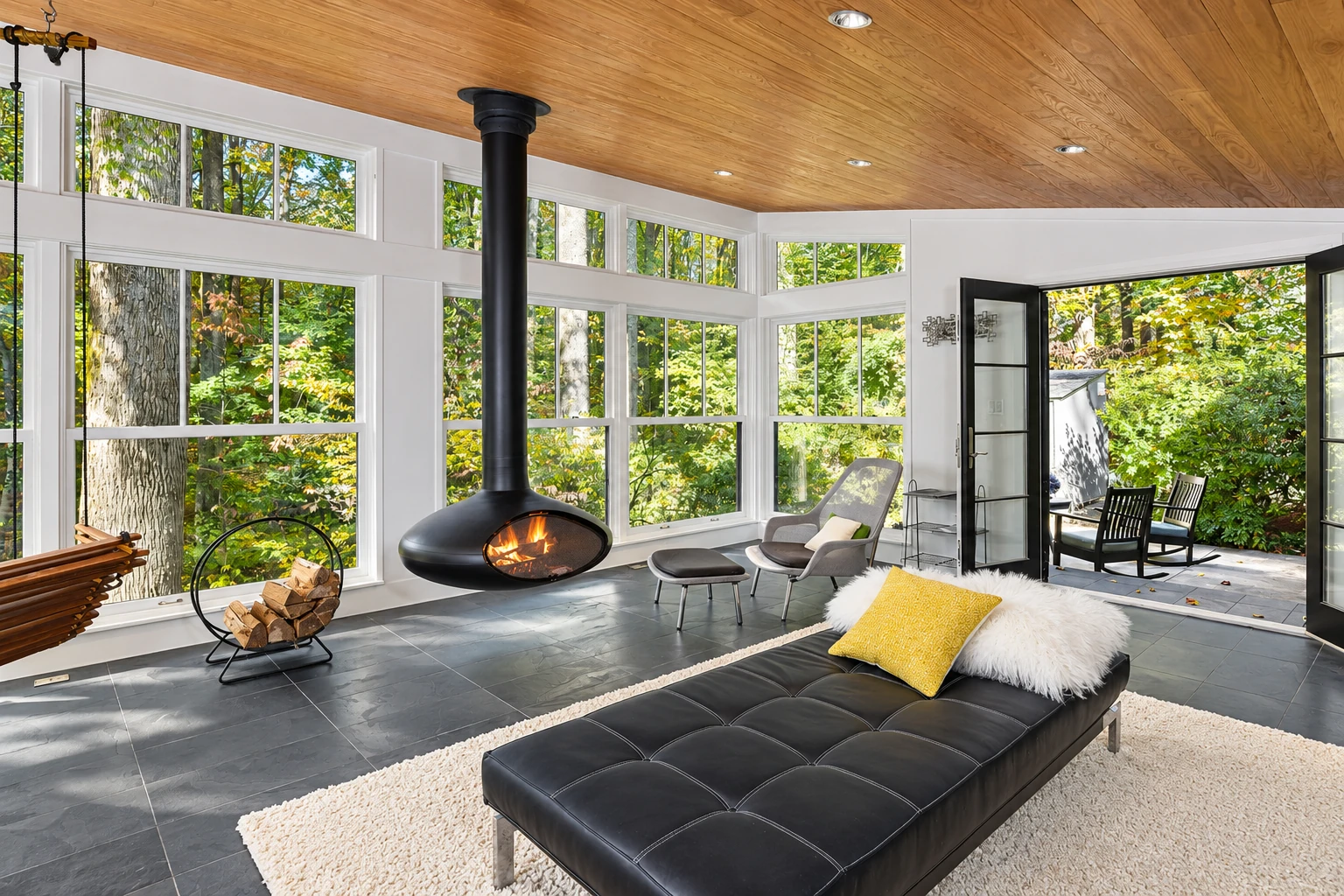 Sunroom with a wood-paneled ceiling, large windows, tiled floor, and a suspended fireplace beside an open patio door.